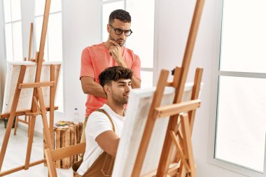 Resim stüdyosunda iki İspanyol erkek öğretmen ve öğrenci çizim yapıyor.