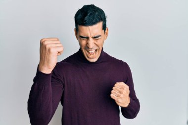 Balıkçı yaka kazak giyen yakışıklı adam kolları havada ve gözleri kapalı bir şekilde başarıyı kutluyor. 