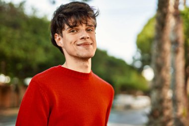 Genç İspanyol adam gülümseyerek şehirde mutlu mesut dikiliyor.