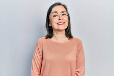 Orta yaşlı İspanyol kadın gündelik kıyafetler ve gözlük takıyor. Pozitif ve mutlu görünüyor. Kendine güvenen bir gülümsemeyle dişlerini gösteriyor. 