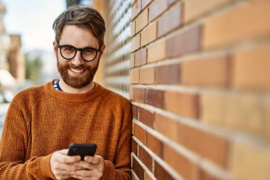 Güneşli bir günde akıllı telefon kullanan sakallı beyaz bir genç adam.