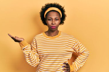 Genç Afro-Amerikalı kadın avuçlarını açmış, elinde kuşkucu ve gergin bir şey tutuyor, sorun yüzünden kaşlarını çatıyor. negatif kişi. 