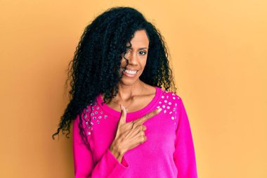Orta yaşlı Afro-Amerikalı kadın, günlük kıyafetler giyiyor. Gülümsüyor, eli ve parmağı yana doğru uzanıyor. 