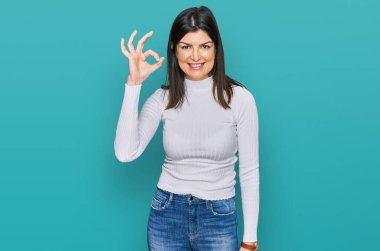 Güzel esmer kadın, günlük kıyafetler giyiyor, gülümsüyor ve el ve parmaklarıyla 