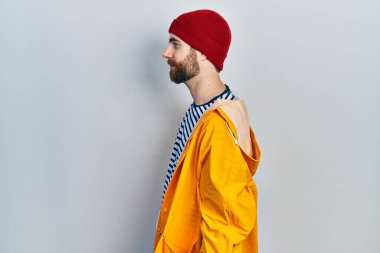 Sakallı, sarı yağmurluk giyen, rahat bir görünüm takınan, doğal yüzlü, kendine güvenen bir gülümseme takınan beyaz bir adam.. 