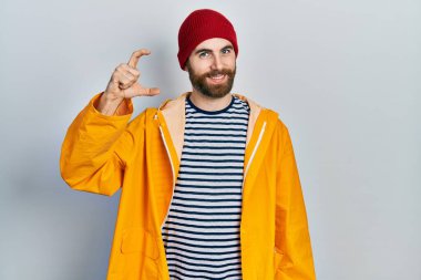 Sakallı, sarı yağmurluk giyen, kendine güvenen, el hareketi yapan, parmaklarıyla işaret yapan ve kameraya bakan beyaz bir adam. ölçüm kavramı. 