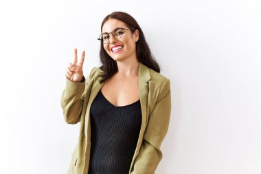 Genç esmer kadın izole edilmiş arka planda duruyor. Gülümsüyor ve parmaklarını zafer işareti yaparken kameraya bakıyor. İki numara.. 
