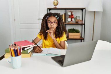 Genç Afro-Amerikan kız evde ödevini yapıyor ve parmakları dudaklarında sessiz olmak istiyor. sessizlik ve gizli konsept. 