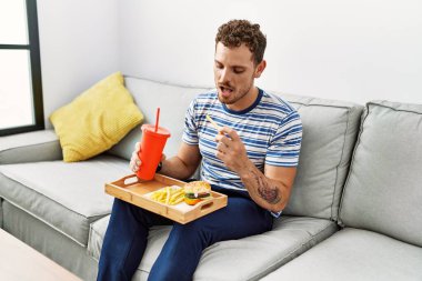 Young hispanic man smiling confident eating classical burger at home
