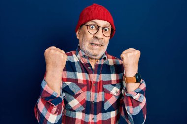 Handsome mature man wearing hipster look with wool cap celebrating surprised and amazed for success with arms raised and open eyes. winner concept. 