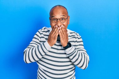 Orta yaşlı, gündelik kıyafetler giyen, gözlüklü, gülen ve utanan bir Latin. Ağzı ellerle, dedikoduyla ve skandal konseptiyle kapatıyor. 