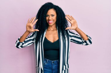 Orta yaşlı Afro-Amerikalı kadın gündelik giysiler giyer ve parmaklarını on numarayla gösterirken kendinden emin ve mutlu bir şekilde gülümserdi.. 