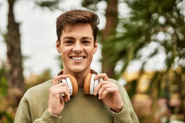 Şehirde kulaklık takarak mutlu gülümseyen genç İspanyol adam..