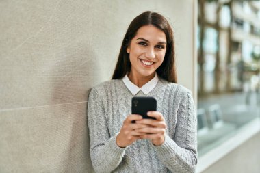Genç İspanyol kadın şehirde akıllı telefon kullanarak mutlu bir şekilde gülümsüyor..
