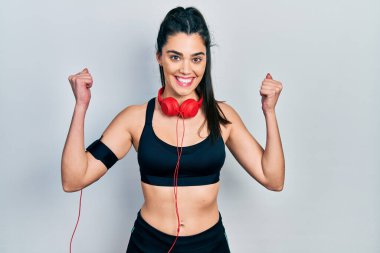 Spor kıyafetleri giyen ve kulaklık takan genç İspanyol kız kollarını kaldırarak ve açık gözlerle başarıyı kutluyor. Kazanan konsept. 