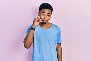 Genç Afro-Amerikalı bir adam günlük mavi tişört giyiyor ağzı ve dudakları parmaklarıyla fermuar gibi kapalı. gizli ve sessiz, tabu konuşması 