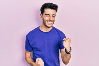 Gündelik tişört giyen genç İspanyol adam kolları havada ve gözleri kapalı bir şekilde başarıyı kutluyor ve şaşırıyor. Kazanan konsept. 