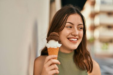Genç beyaz kız gülümseyerek şehirde dondurma yiyor..