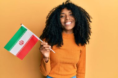 Afro saçlı, Kürdistan bayrağı tutan Afro-Amerikalı kadın pozitif ve mutlu görünüyor ve kendine güvenen bir gülümsemeyle dişlerini gösteriyor. 