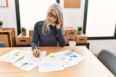 Orta yaşlı, kır saçlı, iş kadını. Ofiste çalışan akıllı telefondan konuşuyor.
