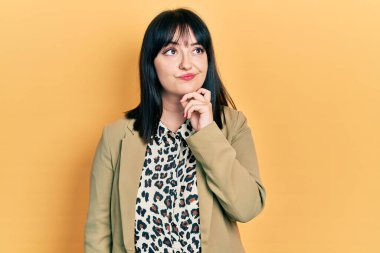 Genç İspanyol kadın iş kıyafetleri giyiyor ciddi yüz ifadesi var eli çenesinde soru soran, kafa karıştırıcı bir fikir hakkında düşünceli. 