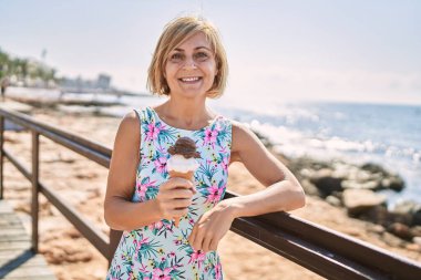 Deniz kenarında dondurma tutan orta yaşlı güzel bir kadın.