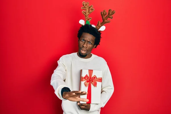 Young African American Man Wearing Deer Christmas Hat Holding Gift — Fotografia de Stock