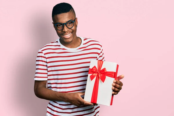 年轻的非洲裔美国人 拿着礼物 站在那里 面带微笑 露出自信的笑容 露出牙齿 看起来积极而快乐 — 图库照片