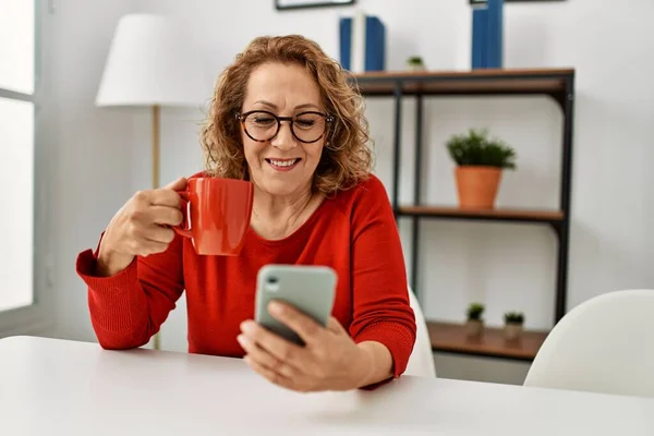 Biała Kobieta Średnim Wieku Używa Smartfona Pije Kawę Siedząc Kanapie — Zdjęcie stockowe