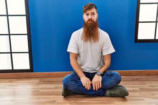 Redhead Man Long Beard Sitting Floor Empty Room Skeptic Nervous — Stok fotoğraf