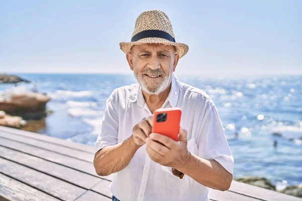 Uomo Anziano Sorridente Fiducioso Indossa Cappello Estivo Utilizzando Smartphone Mare — Foto Stock
