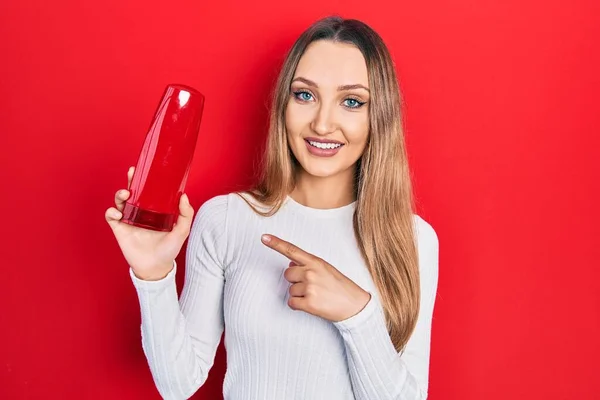 Young Blonde Girl Holding Shampoo Bottle Smiling Happy Pointing Hand — Stok fotoğraf