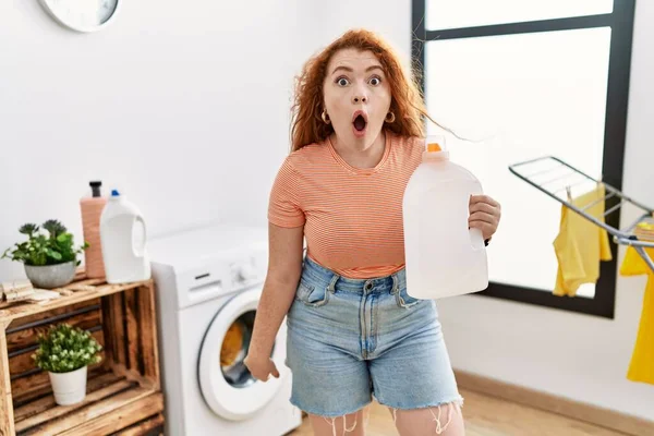 Young Redhead Woman Doing Laundry Holding Detergent Bottle Scared Amazed — Stock Photo, Image