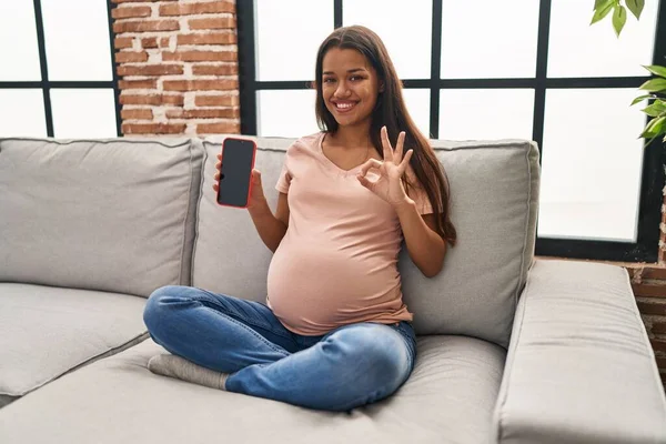Young Pregnant Woman Holding Smartphone Showing Screen Doing Sign Fingers — Stockfoto