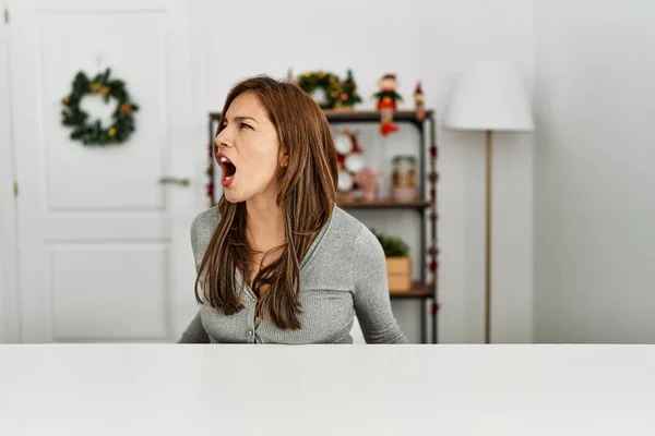 年轻的拉丁女人坐在桌上 被圣诞节装饰得怒气冲冲的 疯狂的尖叫着 气得大喊大叫 愤怒和好斗的概念 — 图库照片