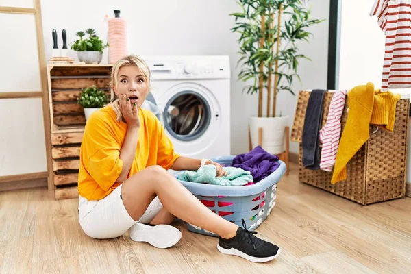 年轻的高加索女人把脏衣服放进洗衣机 满脸恐惧 惊奇和惊奇的表情 — 图库照片
