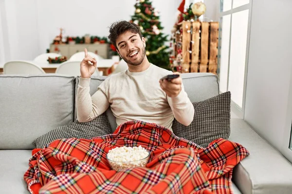 Молодий Іспаномовний Чоловік Їсть Попкорн Сидячи Дивані Різдвяній Ялинці Усміхаючись — стокове фото