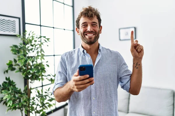 Jovem Homem Bonito Usando Smartphone Casa Sorrindo Com Uma Ideia — Fotografia de Stock