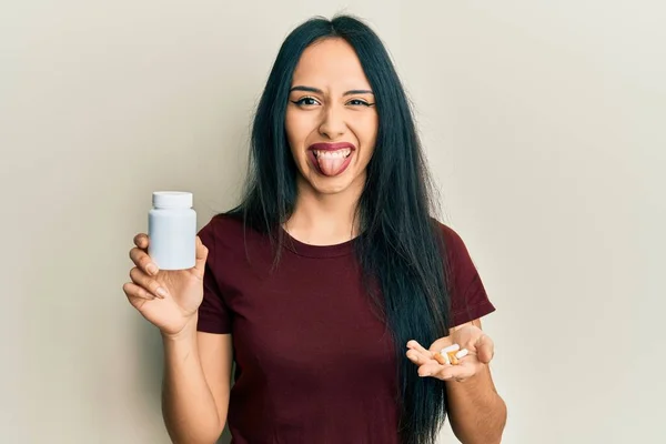 Young Hispanic Girl Holding Pills Sticking Tongue Out Happy Funny — Stockfoto