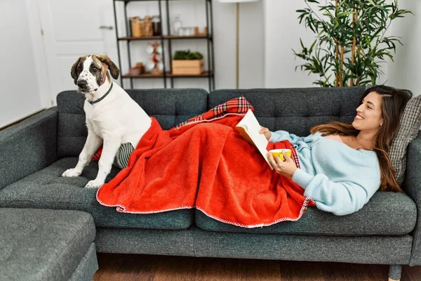 若いです女性読書本と飲み物コーヒー嘘上のソファとともに犬とともに家 — ストック写真