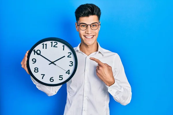 Joven Hispano Sosteniendo Gran Reloj Sonriendo Feliz Señalando Con Mano — Foto de Stock