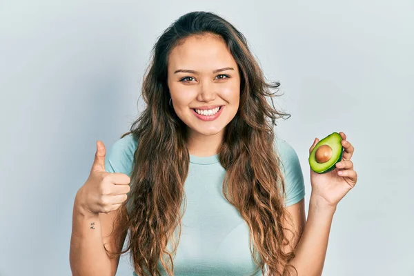 Молодая Латиноамериканка Держит Средний Авокадо Улыбаясь Счастливый Позитивный Большой Палец — стоковое фото