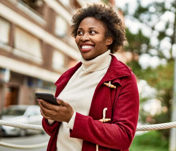 アフロの髪を持つ美しいビジネスアフリカ系アメリカ人女性は スマートフォンを使用して街で幸せと自信を持って屋外で笑顔 — ストック写真