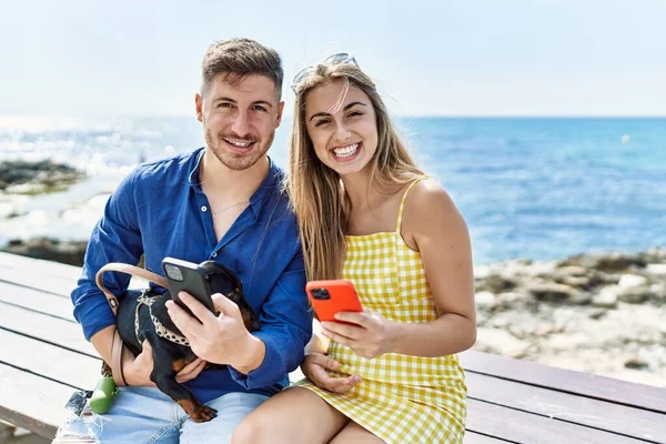 Unga Kaukasiska Par Använder Smartphone Sitter Bänken Med Hund Stranden — Stockfoto