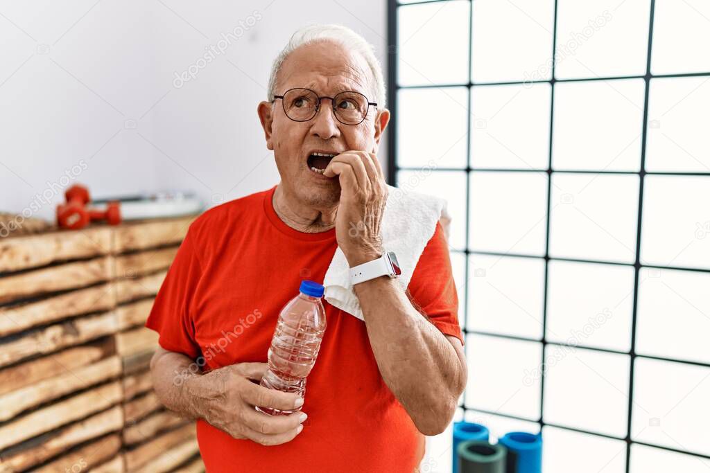 Senior man wearing sportswear and towel at the gym looking stressed and nervous with hands on mouth biting nails. anxiety problem. 
