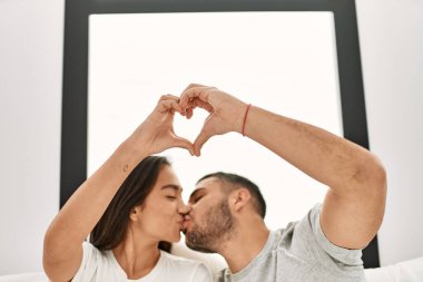 Genç İspanyol çift kalp sembolü yapıyor. Elleri yatakta oturuyor..