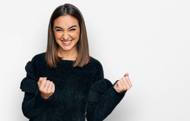 Beautiful brunette woman wearing elegant sweater excited for success with arms raised and eyes closed celebrating victory smiling. winner concept. 