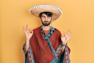 Young hispanic man holding mexican hat relax and smiling with eyes closed doing meditation gesture with fingers. yoga concept. 