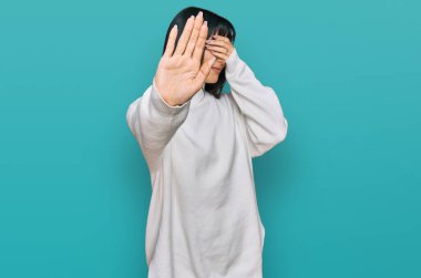 Young brunette woman with bangs wearing casual turtleneck sweater covering eyes with hands and doing stop gesture with sad and fear expression. embarrassed and negative concept. 
