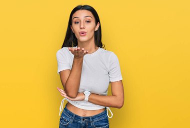 Latin asıllı genç bir kız, günlük beyaz tişörtler giyip kameraya bakıyor ve havada bir öpücük savuruyor. Güzel ve seksi. aşk ifadesi. 